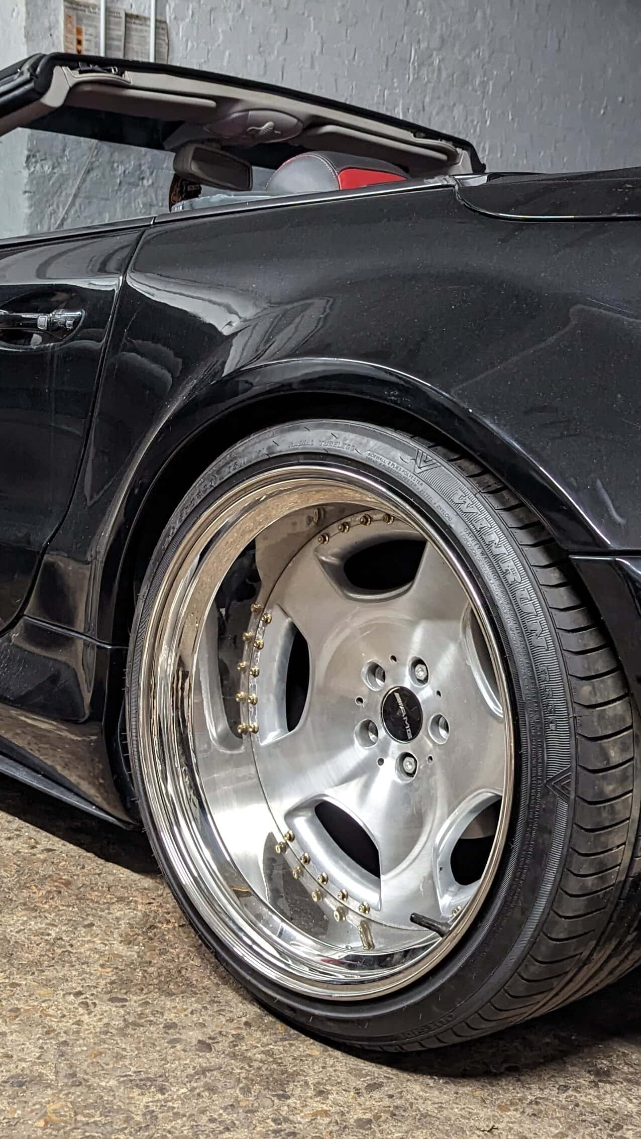 Black Mercedes SL on polished split-rim wheels, inside the Rootes Motors workshop